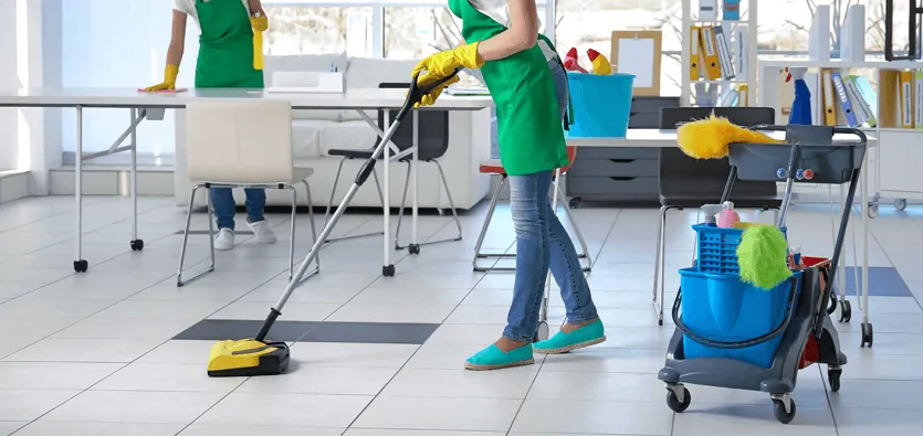 Cleaning crew sweeping tile floors and wiping desks in a commercial office